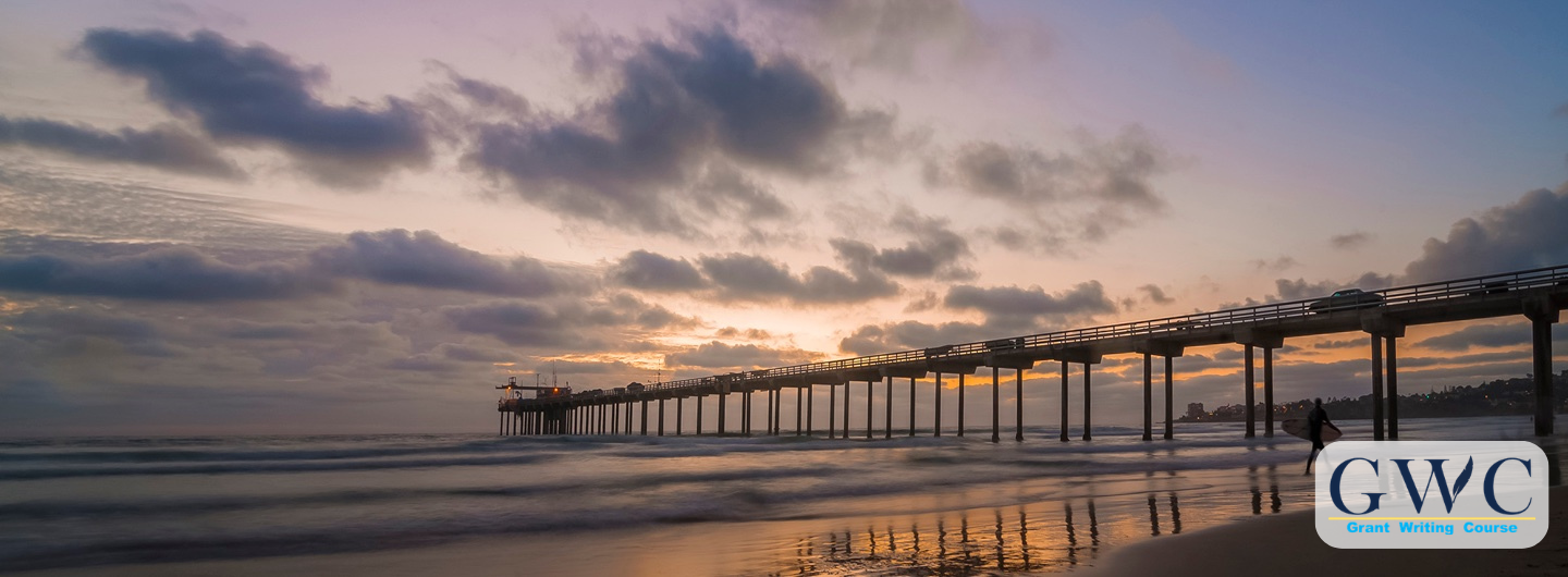 The Scripps Institution of Oceanography pier at dusk with surfer in foreground. 